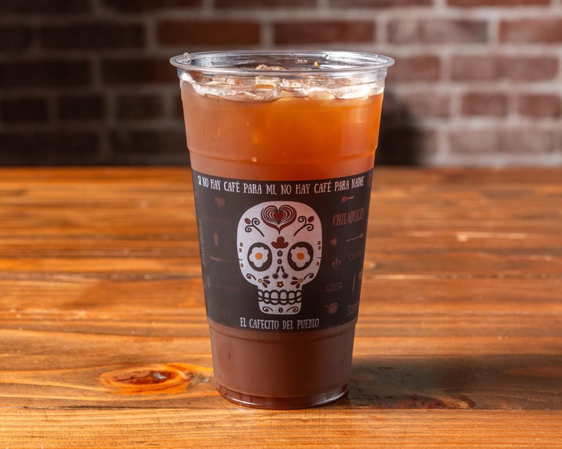 Iced coffee in a clear plastic cup with a decorative sugar skull label on a wooden table.