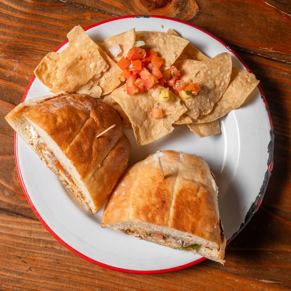 Two halves of a sandwich with chips and pico de gallo on a white plate with a red rim.