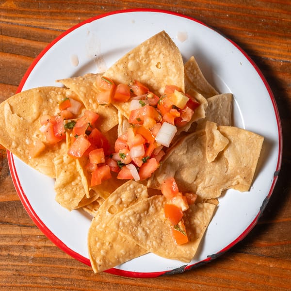 Crispy tortilla chips topped with fresh pico de gallo on a white plate with a red rim.