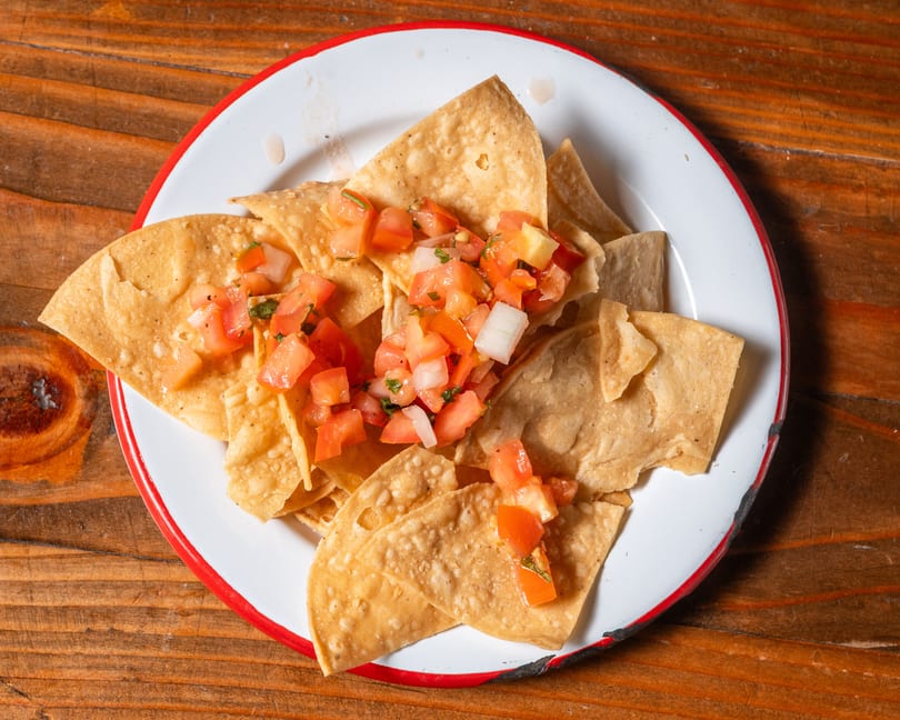 Crispy tortilla chips topped with fresh pico de gallo on a white plate with a red rim.