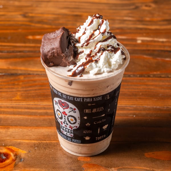 A chocolate milkshake with whipped cream, chocolate drizzle, and a chocolate bar on a wooden table.