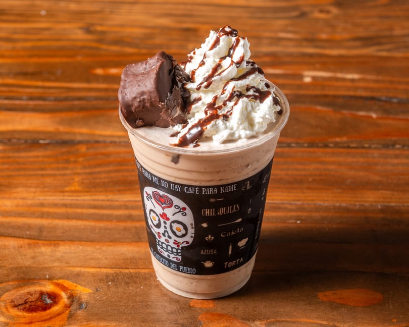 A chocolate milkshake with whipped cream, chocolate drizzle, and a chocolate bar on a wooden table.