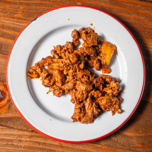 A white plate with a red rim holds a serving of saucy, chopped meat and pineapple chunks.