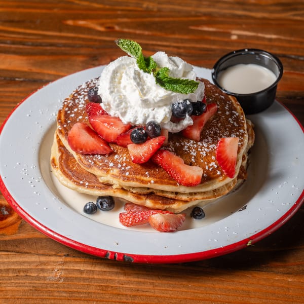 Stack of pancakes topped with whipped cream, strawberries, blueberries, and powdered sugar.
