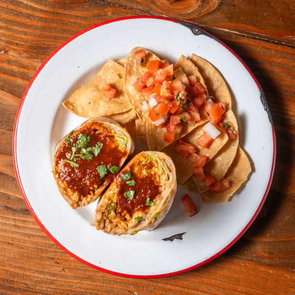 Two halves of a burrito topped with red sauce and cilantro, served with tortilla chips and pico de gallo.