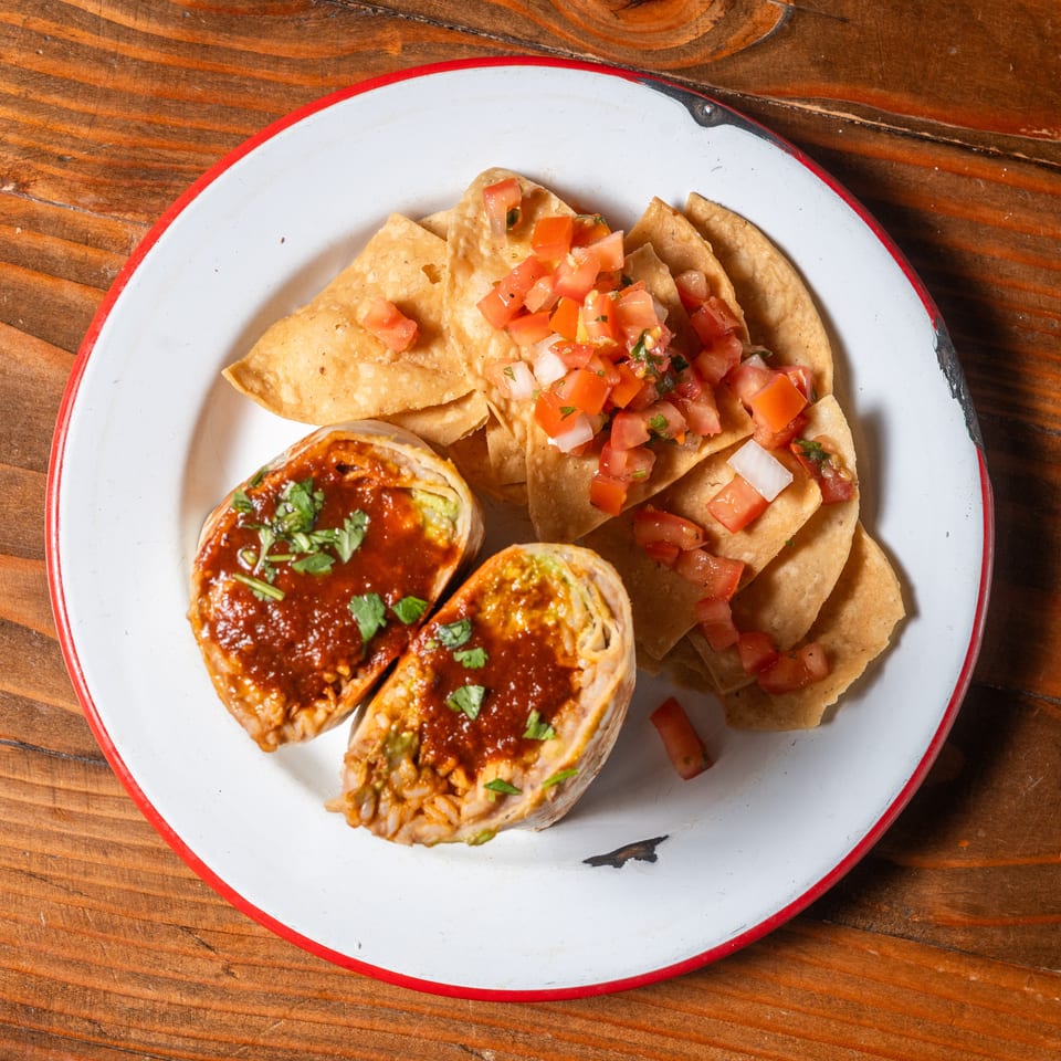Two halves of a burrito topped with red sauce and cilantro, served with tortilla chips and pico de gallo.