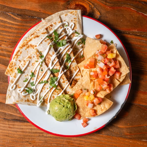 Quesadillas drizzled with sour cream and cilantro, with tortilla chips, salsa, and guacamole.