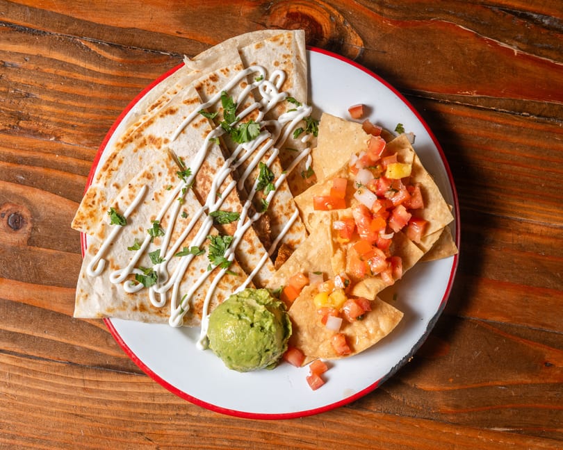 Quesadillas drizzled with sour cream and cilantro, with tortilla chips, salsa, and guacamole.