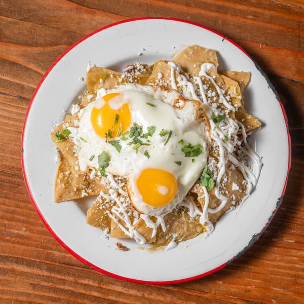 Chilaquiles with green sauce, two fried eggs, cheese, and crema on a white plate.