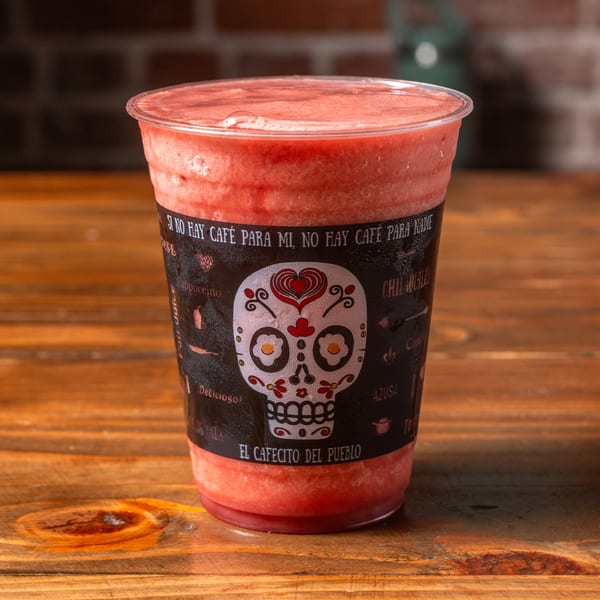 A vibrant red smoothie in a clear cup with a decorative black sleeve featuring a sugar skull design.