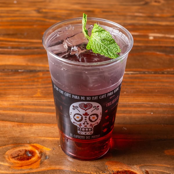 A vibrant red drink with ice and mint in a clear cup with a decorative skull logo.