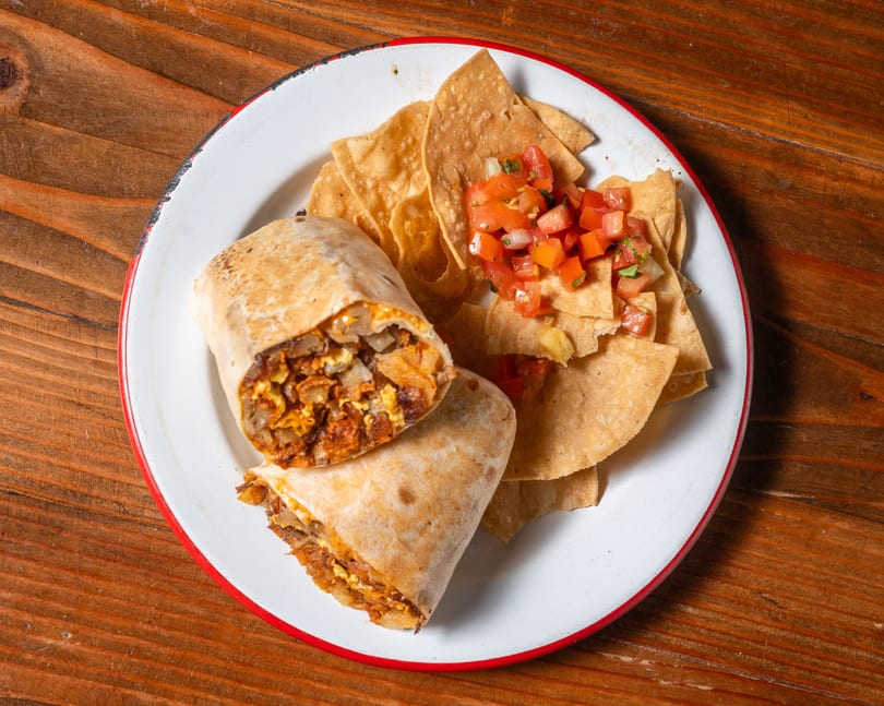 A chorizo and egg breakfast burrito, cut in half, served with tortilla chips and pico de gallo.