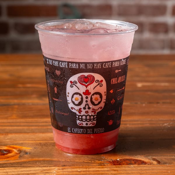 A cold pink drink in a clear plastic cup with a decorative sleeve featuring a sugar skull design.