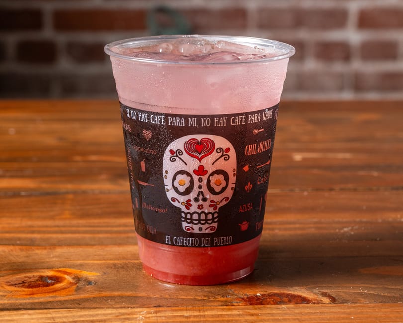 A cold pink drink in a clear plastic cup with a decorative sleeve featuring a sugar skull design.