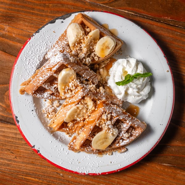 Waffles topped with bananas, granola, powdered sugar, syrup, and whipped cream with mint.