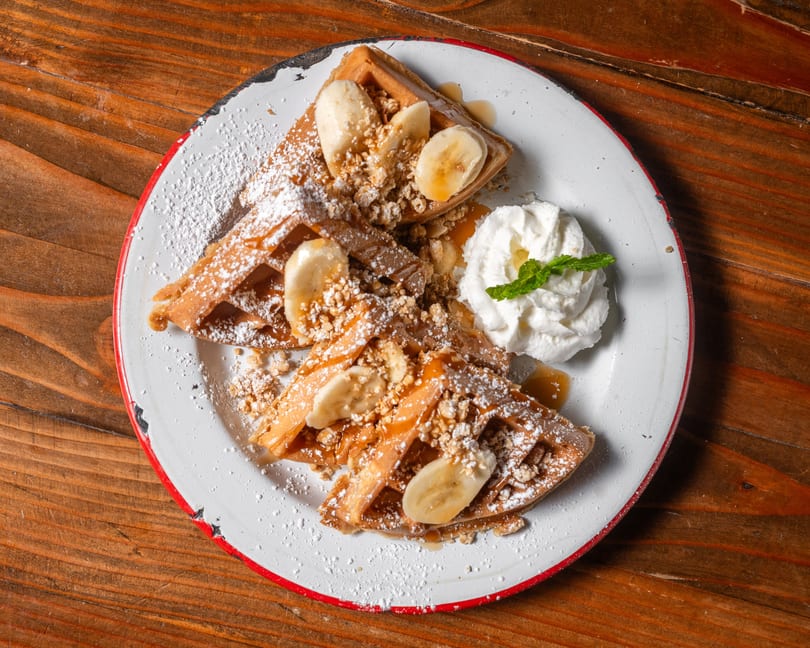 Waffles topped with bananas, granola, powdered sugar, syrup, and whipped cream with mint.