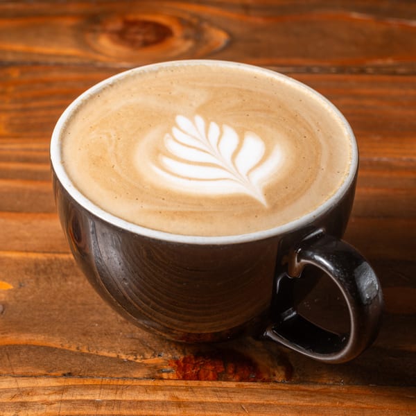 A dark coffee mug filled with latte art, featuring a delicate leaf design in the foam.
