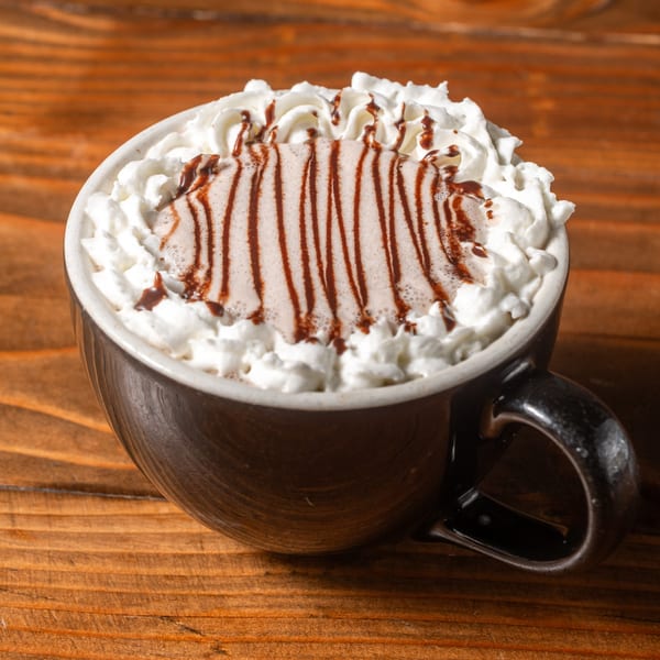 A dark mug of hot chocolate topped with whipped cream and chocolate syrup on a wooden table.