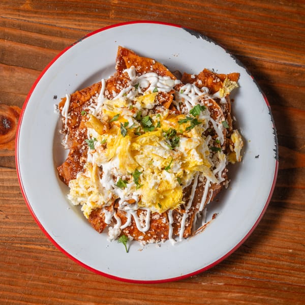 Chilaquiles with red sauce, scrambled eggs, sour cream, cheese, and cilantro on a white plate.